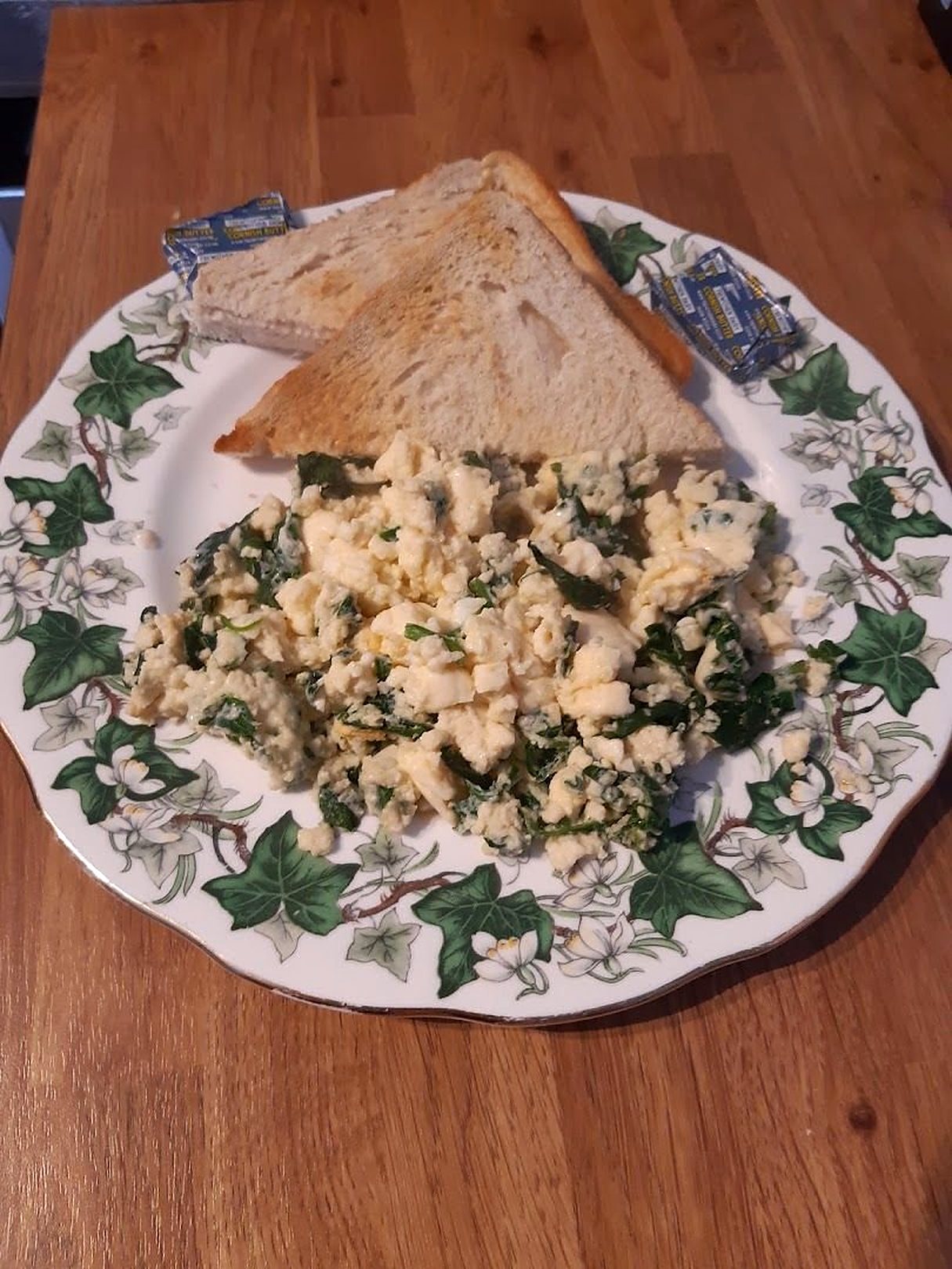 Scrambled eggs with greens and toast on an ivy-patterned plate