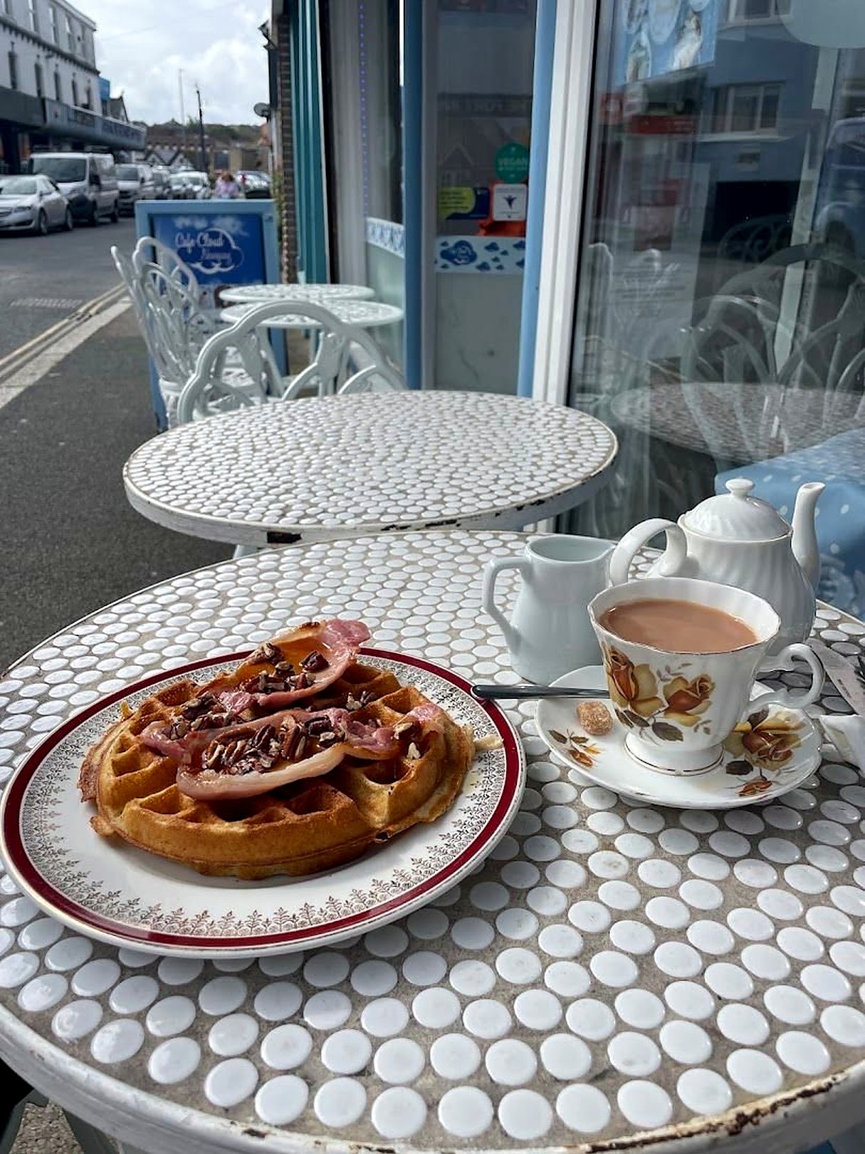 A homemade waffle and a pot of tea on a mosaic bistro table outside the café